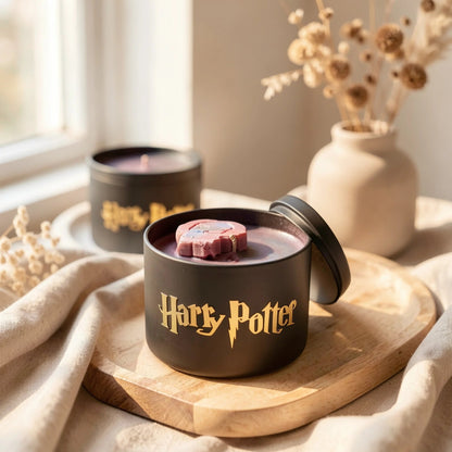 Two 'Harry Potter' themed black containers with gold text on a wooden surface, one containing a pink treat.