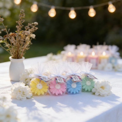 Pastel-colored flower-shaped soaps on a table with string lights in the background