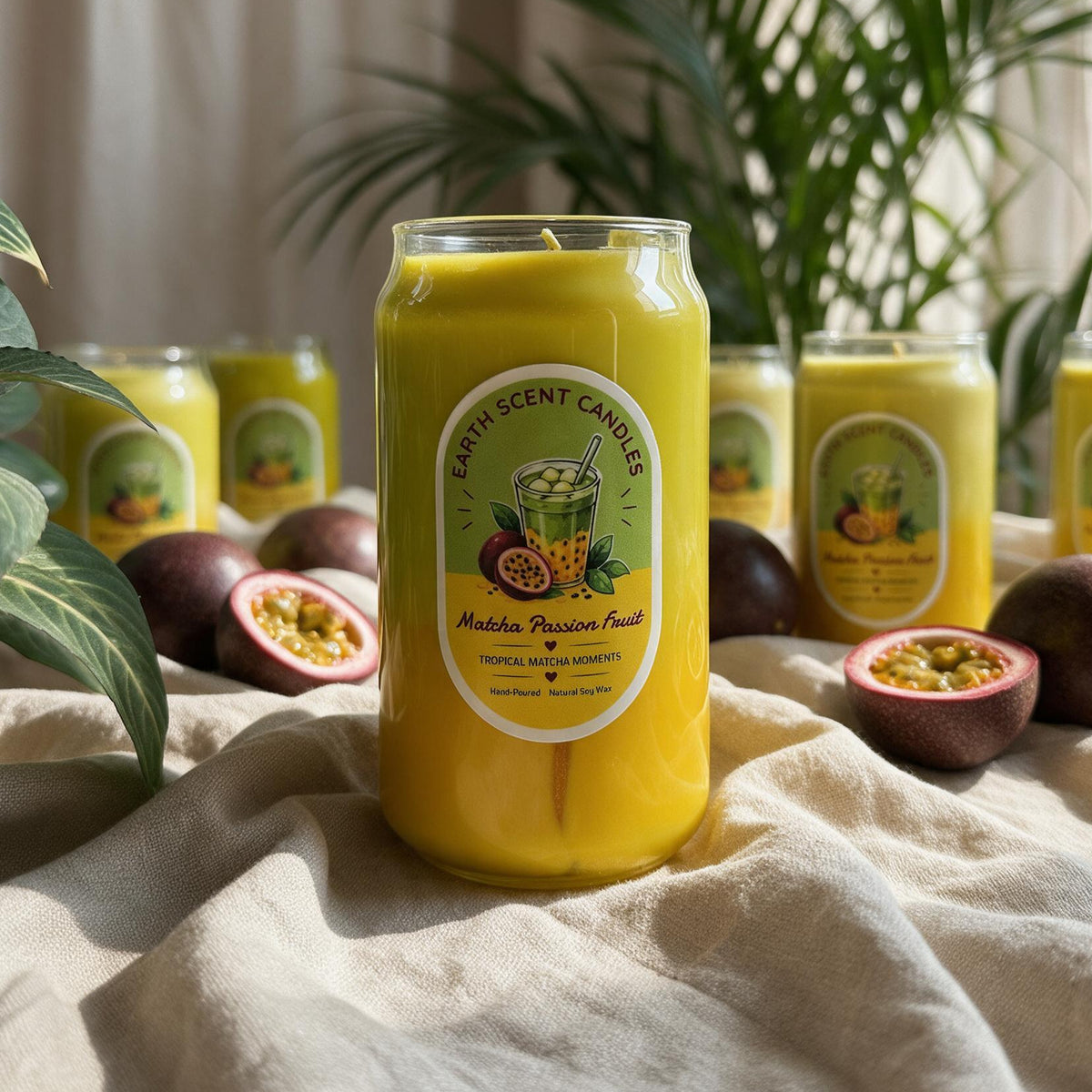 A yellow jar candle labeled 'Earth Scent Candles' and 'Middle Passage Fruit' is displayed on draped beige fabric, surrounded by passion fruit and other matching candles in the background with green plants.